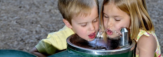 Kids drinking water from a public fountain